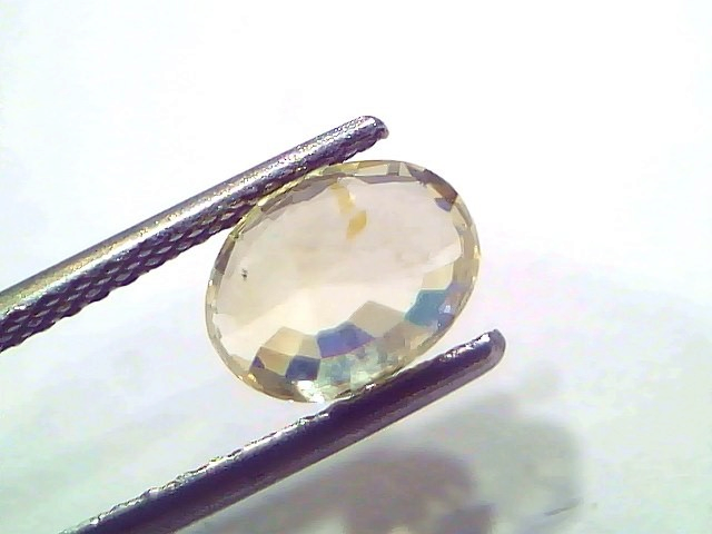Oval-shaped 2.55 Ct certified unheated natural Ceylon yellow sapphire held with tweezers, showcasing its brilliant facets.