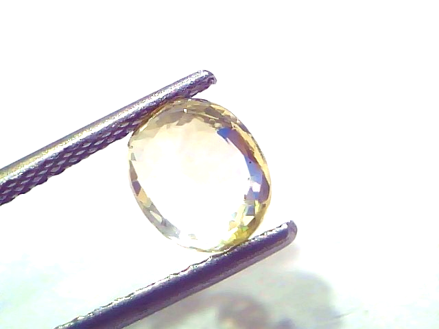 Oval-shaped 2.15 Ct certified unheated natural Ceylon yellow sapphire held by tweezers, showcasing its vibrant yellow hue.