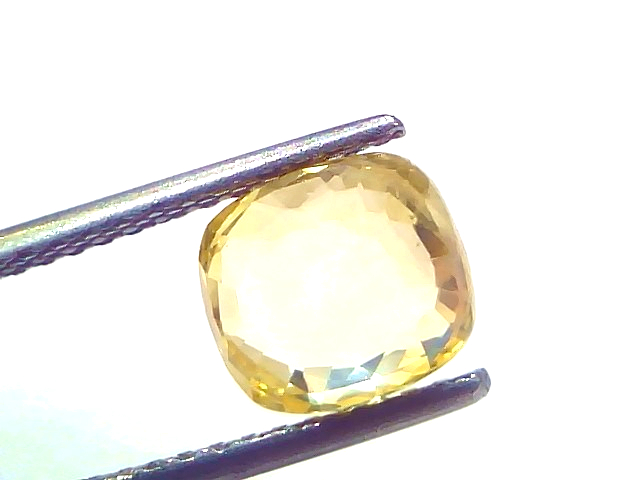 Ceylon yellow sapphire gemstone, 3.24 carats, cushion cut, held by tweezers against a white background.