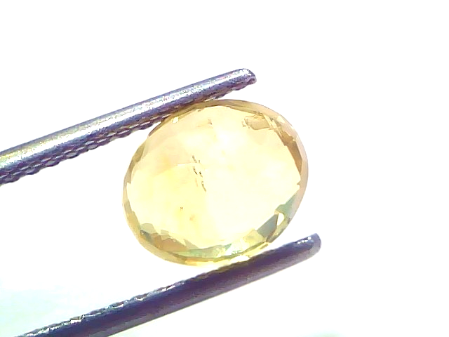 3.20 carat IGI certified unheated natural Ceylon yellow sapphire, oval cut, held with tweezers against a white background.
