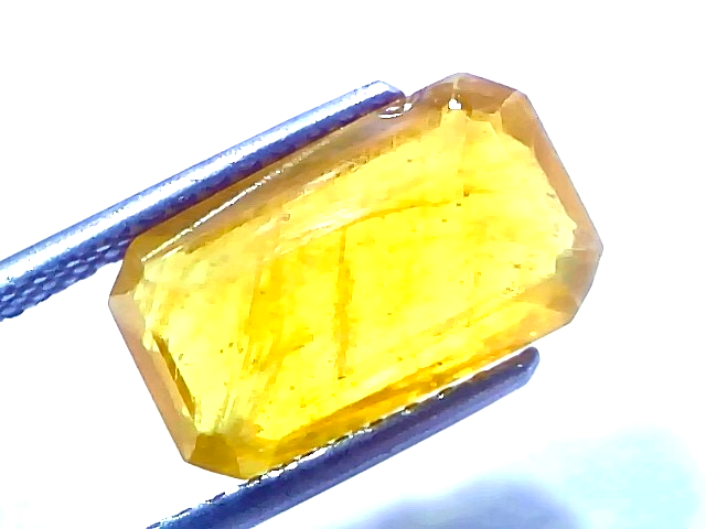 6.94 carat certified natural yellow sapphire Pukhraj stone, heated, displayed in tweezers, showcasing its vibrant yellow hue.