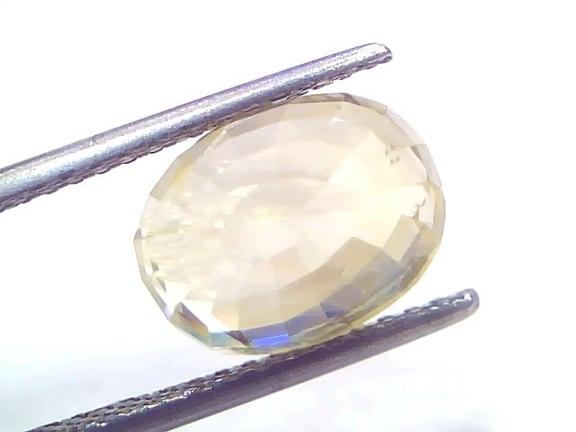 7.30 Ct Certified Unheated Natural Ceylon Yellow Sapphire Pukhraj – 8 Ratti, oval-shaped gemstone held by tweezers, showcasin