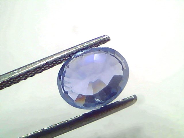 Oval-shaped 2.99 carat unheated natural Ceylon blue sapphire held by tweezers, showcasing its vibrant blue color and facets.