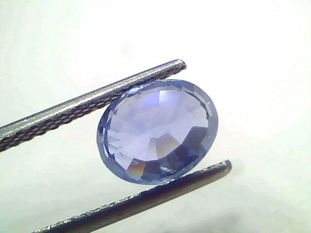 Oval-shaped 2.99 carat unheated natural Ceylon blue sapphire held by tweezers, showcasing its vibrant blue color and facets.